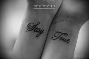 Фото татуировки с надписью "Stay True" на запястьях. Рисунок выполнен в черном цвете с использованием каллиграфического шрифта.
