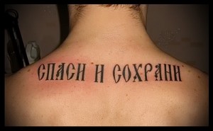 Фото тату надписи «Спаси и сохрани» на спине мужчины, выполненной черными чернилами. Религиозная татуировка, выражающая веру и надежду.
