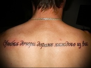 Фото тату на спине с надписью на русском языке: "Улыбка дочери дороже каждого из вас". Элегантный эскиз тату в красных тонах, выражающий любовь к ребенку.