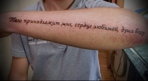 Фото тату на предплечье с надписью на русском языке: "Тело принадлежит мне, сердце любимой, душа Богу". Элегантный эскиз тату в красных тонах.