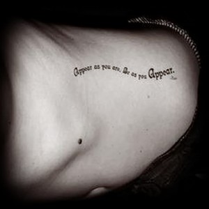 Фотография черно-белой татуировки с фразой 'Appear as you are. Be as you appear.' на боку женщины.