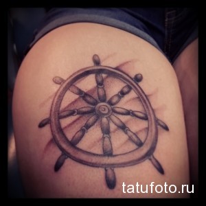 Простая черно-серая татуировка на плече с изображением штурвала, выполненная в минималистичном стиле.