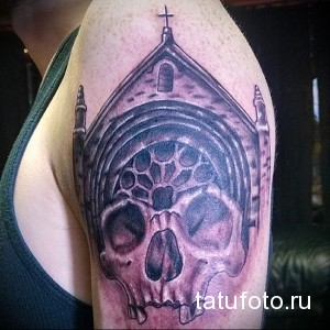 Черно-серая татуировка на плече с изображением черепа, заключенного в архитектурную структуру, напоминающую храм или собор.
