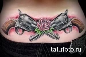 Татуировка на животе с изображением двух скрещенных револьверов и розой между ними.