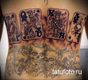 Фото тату: большая татуировка на спине, состоящая из игральных карт, черепов, надписей и других символов. Сложный и детализированный дизайн.