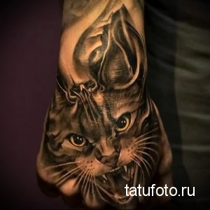 Фото реалистичной татуировки кошачьей морды, покрывающей тыльную сторону руки. Детализированный рисунок татуировки с желтыми глазами.