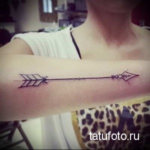 Фото тату: изящная стрела, выполненная тонкими линиями, украшает предплечье девушки. Идеальный выбор для тех, кто ценит минимализм и символизм.