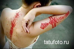 Фото тату в стиле трайбл на спине и руке девушки. Красный рисунок татуировки с геометрическими узорами.