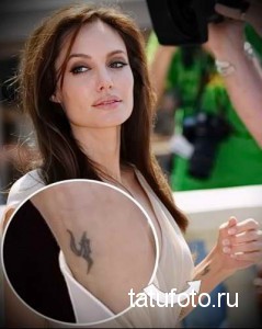 Фотография Анджелины Джоли с татуировкой в виде темных символов на руке. Крупный план тату, демонстрирующий детали рисунка.