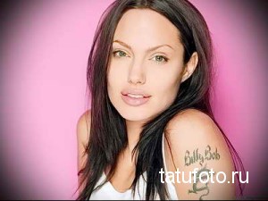 Фотография Анджелины Джоли с татуировкой надписи на плече. Крупный план тату, демонстрирующий текст и стиль шрифта.