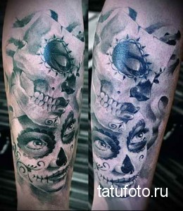 Фото тату на предплечье в стиле сахарной смерти (sugar skull): черепа, украшенные цветами и узорами. Черно-белая татуировка с голубыми акцентами.