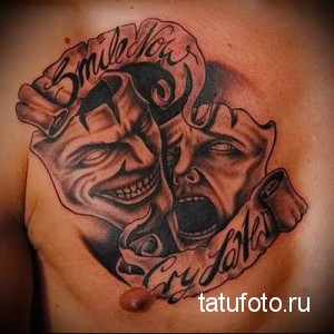 Фото тату на груди с изображением двух театральных масок: смеха и плача. Черно-белая татуировка с надписью 'Smile now, cry later'.