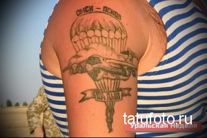 Фото тату парашюта с самолетом и надписью 'Диск - Лебедь' на плече мужчины. Черно-серый рисунок татуировки в стиле олдскул.