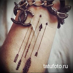 Фото тату на запястье с изображением нескольких минималистичных стрел и логотипа Chanel. Небольшой рисунок татуировки черным цветом.