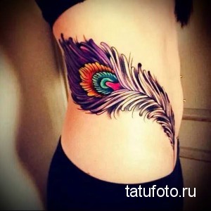Цветная татуировка на боку изображает павлинье перо с яркими и насыщенными цветами. Детализированный рисунок татуировки с использованием различных оттенков и текстур.