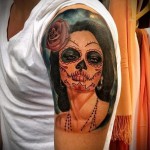 Фото тату на плече: девушка в стиле Sugar Skull с розой в волосах, выполненная в ярких цветах.