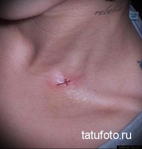 Фото татуировки с небольшим красным крестом на груди мужчины. Рисунок выполнен в минималистичном стиле.