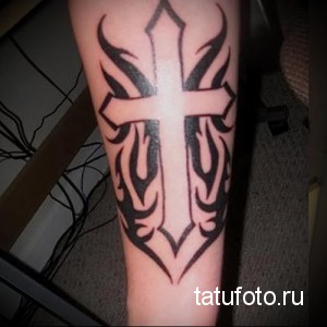 Фото тату: татуировка в стиле tribal с изображением креста, окруженного языками пламени. Черно-белый рисунок с четкими линиями и геометрическими узорами.