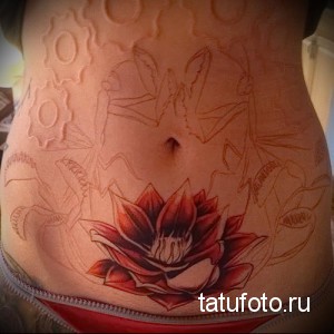 Фото тату: большой цветок лотоса, расположенный на женском животе, с элементами механического стиля. Оригинальный и запоминающийся рисунок.