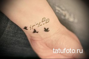 Фото тату трех маленьких птиц и надписи "if you're a bird, I'm a bird" на запястье. Черный рисунок татуировки, символизирующий свободу и любовь.