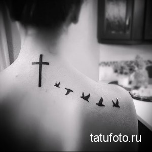 Фото тату на спине: крест и летящие птицы, выполненные в черном цвете, символизирующие веру, надежду и свободу.