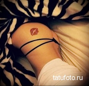 Фото тату: яркий красный отпечаток губ на бедре девушки. Интимное расположение, четкие контуры.