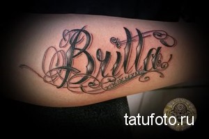 Фото тату надписи 'Bulldog' на предплечье, выполненной в черно-серой гамме с декоративными элементами и римскими цифрами.