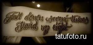 Фото тату на руке с надписью "Fall down seven times, stand up eight" выполненной красивым шрифтом.