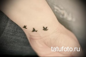 Фото тату трех маленьких птиц на запястье руки. Черно-белый рисунок, выполненный в минималистичном стиле.
