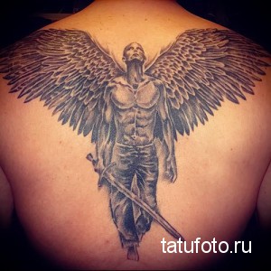 Фото тату ангела с мечом на спине. Черно-серая татуировка, детализированные крылья, воинственный ангел, реалистичный стиль.