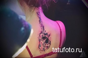 Фото тату акварельного черепа с гитарой на спине. Нежные розовые, голубые и фиолетовые оттенки, брызги краски, создающие эффект меланхолии и романтики.