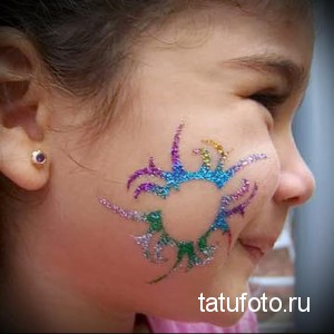 Фото татуировки в виде красочного краба, нанесенной на щеку. Блестящий рисунок татуировки с использованием разных цветов.