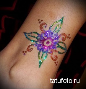 Фото тату с изображением цветка, выполненного из разноцветных блесток на лодыжке. Нежный и яркий рисунок для девушек.