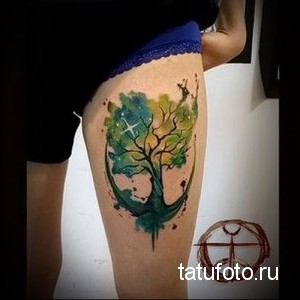Фото тату: акварельное дерево жизни на бедре. Зеленые и синие оттенки, звездное небо, символизм.