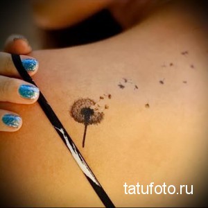 Фото тату одуванчика на лопатке. Маленький, детально прорисованный рисунок с летящими пушинками, выполненный в коричневых тонах.