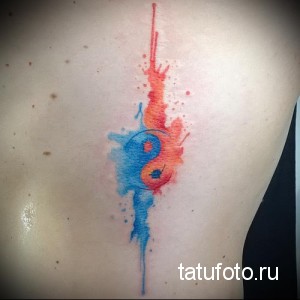 Фото тату: акварельный символ Инь и Ян на спине. Красные и синие оттенки, брызги краски, гармония.