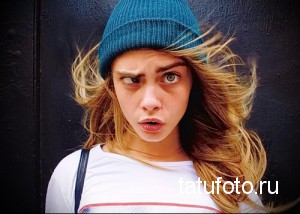 Фотография Кары Делевинь в вязаной шапке, с приподнятой бровью и растрепанными волосами. На фоне темная стена.