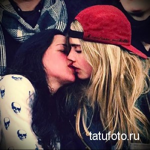 Фотография двух девушек, страстно целующихся. На одной из девушек красная бейсболка, на другой - белая кофта с черепами. Изображение передает атмосферу любви и свободы.