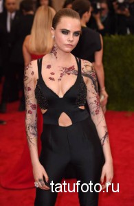 Фото тату: Cara Delevingne демонстрирует татуировку в стиле ирреалистичной сакуры, покрывающую шею, плечи и руки, вид спереди.