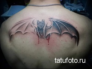 Фото тату на спине с изображением летучей мыши, из которой капают капли крови. Готический стиль, темные тона, детализированный рисунок.