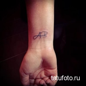 Фото тату инициалов "AB" на запястье, выполненных изящным шрифтом. Татуировка имеет минималистичный и элегантный вид.