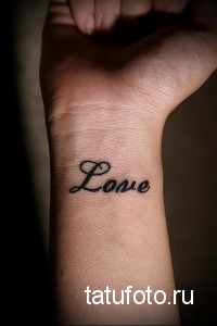 Фото тату: надпись 'Love' красивым шрифтом на запястье. Минималистичная татуировка с черными чернилами, популярный выбор для пар.