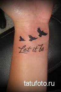 Фото татуировки с изображением трех летящих птиц и надписи 'Let it be' на запястье. Черно-белый рисунок татуировки, выполненный в минималистичном стиле.