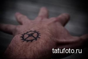 Черно-белое фото татуировки на ладони с изображением сложного геометрического символа, напоминающего шестеренку или магический знак.