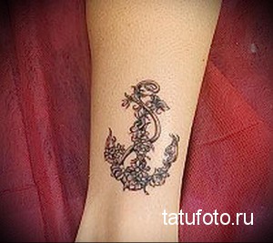 Фото тату: татуировка якоря, обвитого цветами и растительными узорами, на женском запястье. Черно-белый рисунок.