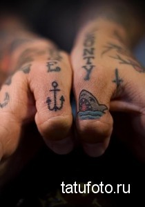 Фото тату на пальцах: маленькие изображения якоря и акулы, выполненные в черном цвете с добавлением голубых оттенков.