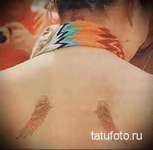 Фото тату хной на спине, изображающее два крыла с яркими перьями в оранжевых и бирюзовых тонах, выполненное в акварельном стиле.