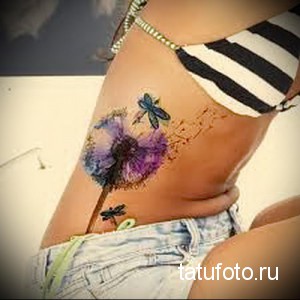 Фото тату акварельного одуванчика и стрекозы на боку. Яркие, красочные краски и нежные мазки создают эффект легкости и воздушности.