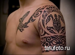 Фото тату: большая черно-белая татуировка в полинезийском стиле на плече и груди. Детализированный рисунок с изображением маски и морского существа.