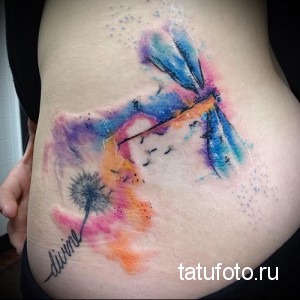 Фото тату: Акварельная татуировка стрекозы и одуванчика на боку, выполненная в нежных голубых, розовых и фиолетовых тонах с использованием техники размытия.